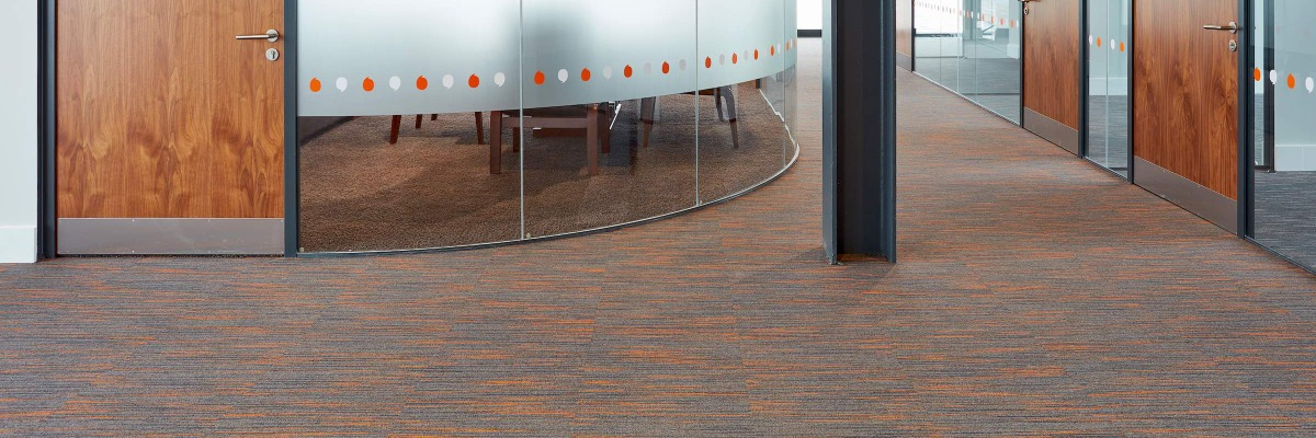 Image of office flooring with the door and glass of a private office in he background.